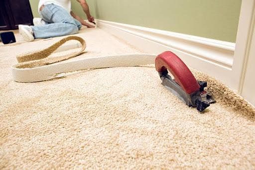 Professional carpet installer in kneepads using precision trimmer along baseboard moldings