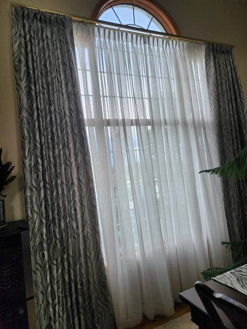 High-Arch Two-Storey Custom Sheer Curtains & Drapery - Window Coverings by Deluxe in Calgary Residence. Grand two-storey cathedral arched window treatment featuring pinch-pleated linen sheers and elegant jacquard drapery side panels with custom curved track hardware.