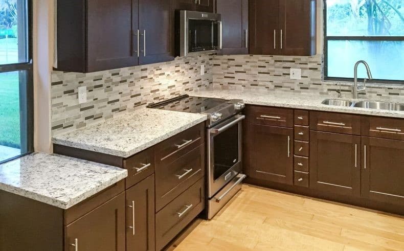 Horizontal linear iridescent glass mosaic kitchen backsplash tiles behind polished granite countertops