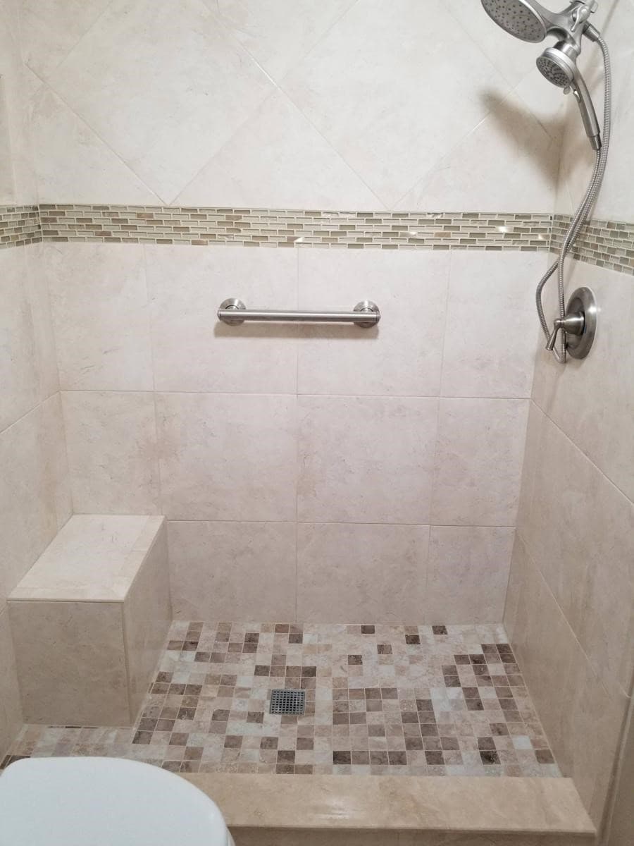 Curbless walk-in porcelain shower enclosure featuring a built-in corner bench and mosaic stone floor pan