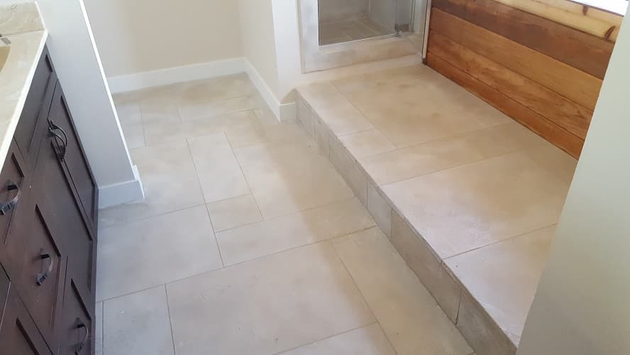 Large-format honed porcelain bathroom floor tiles with a raised walk-in shower threshold step