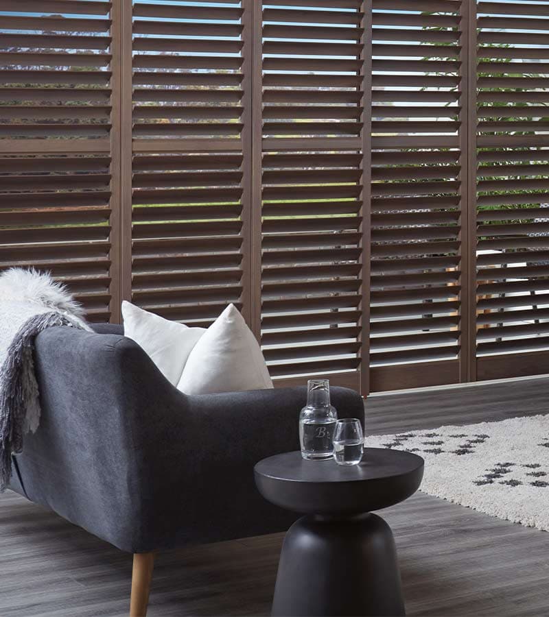 Rich walnut-stained hardwood plantation shutters mounted on an overhead sliding bypass track