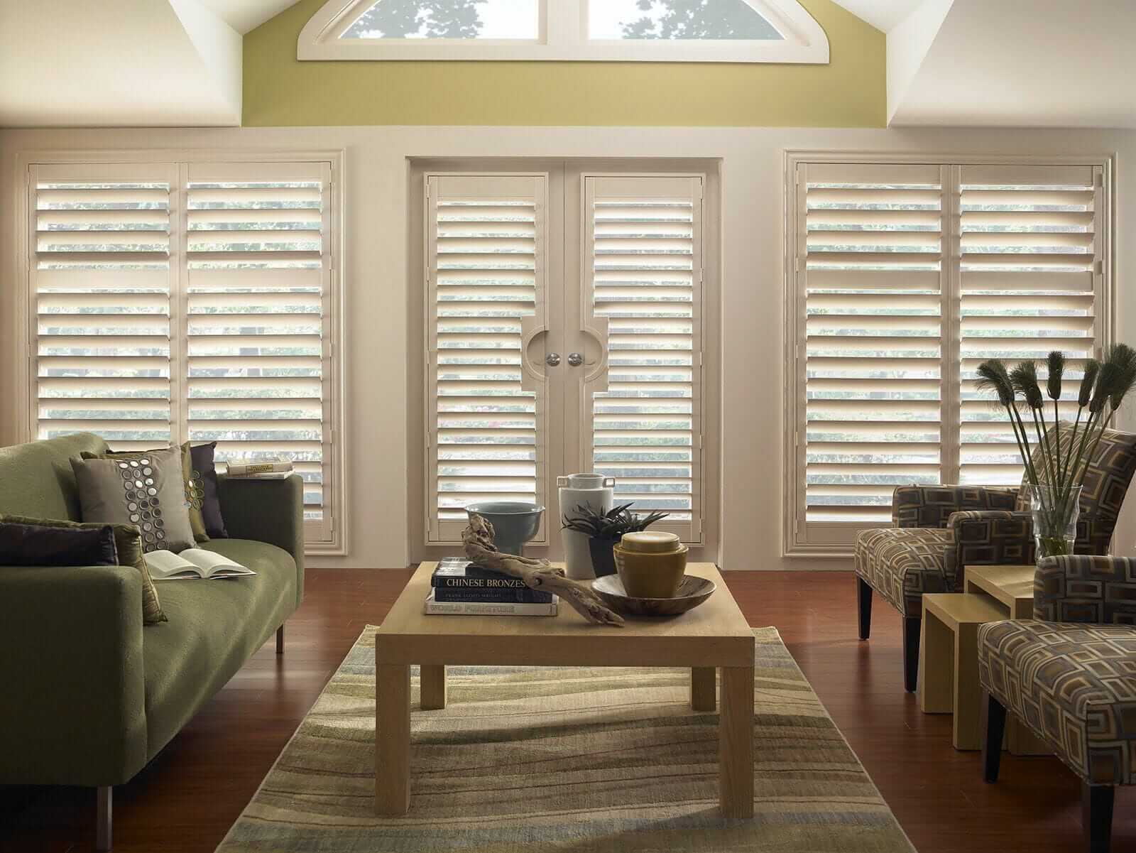 Off-white custom wood plantation shutters with divider rails framing living room windows and French doors